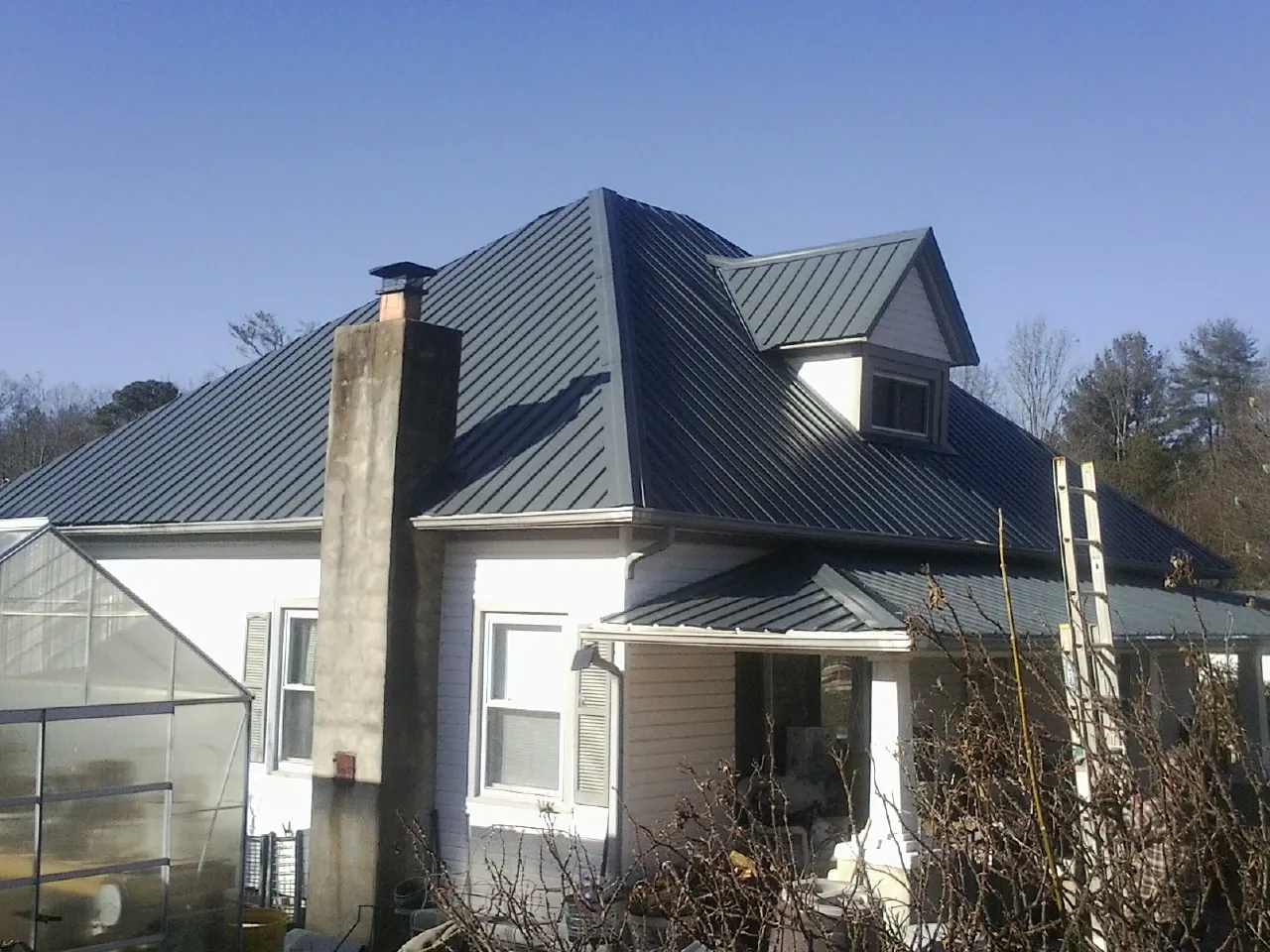 Dark blue standing seam metal roof on a white farmhouse with dormer — Slate & Tile Roof Repair by Roofing Brothers in Cushing