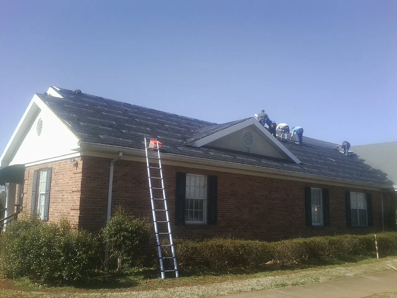 Crew tearing shingles off a brick ranch roof with a ladder set — Emergency Roof Repair work by our crew in Cushing
