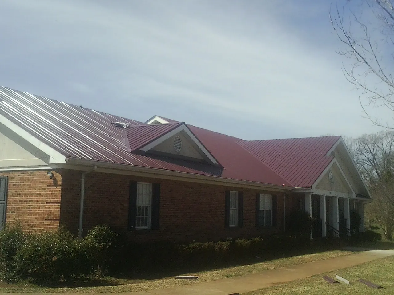 Red metal roof with gabled entries on a long brick building, from a Hail Damage Roof Repair job in Cushing