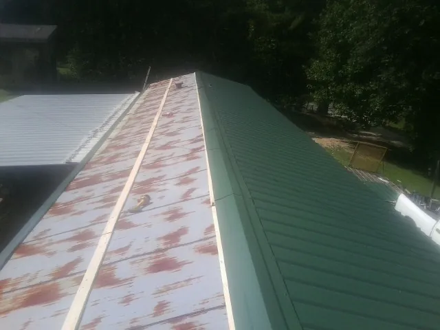 Old rusted panels beside newly installed green metal roofing — Wind Damage Roof Repair by Roofing Brothers in Cushing