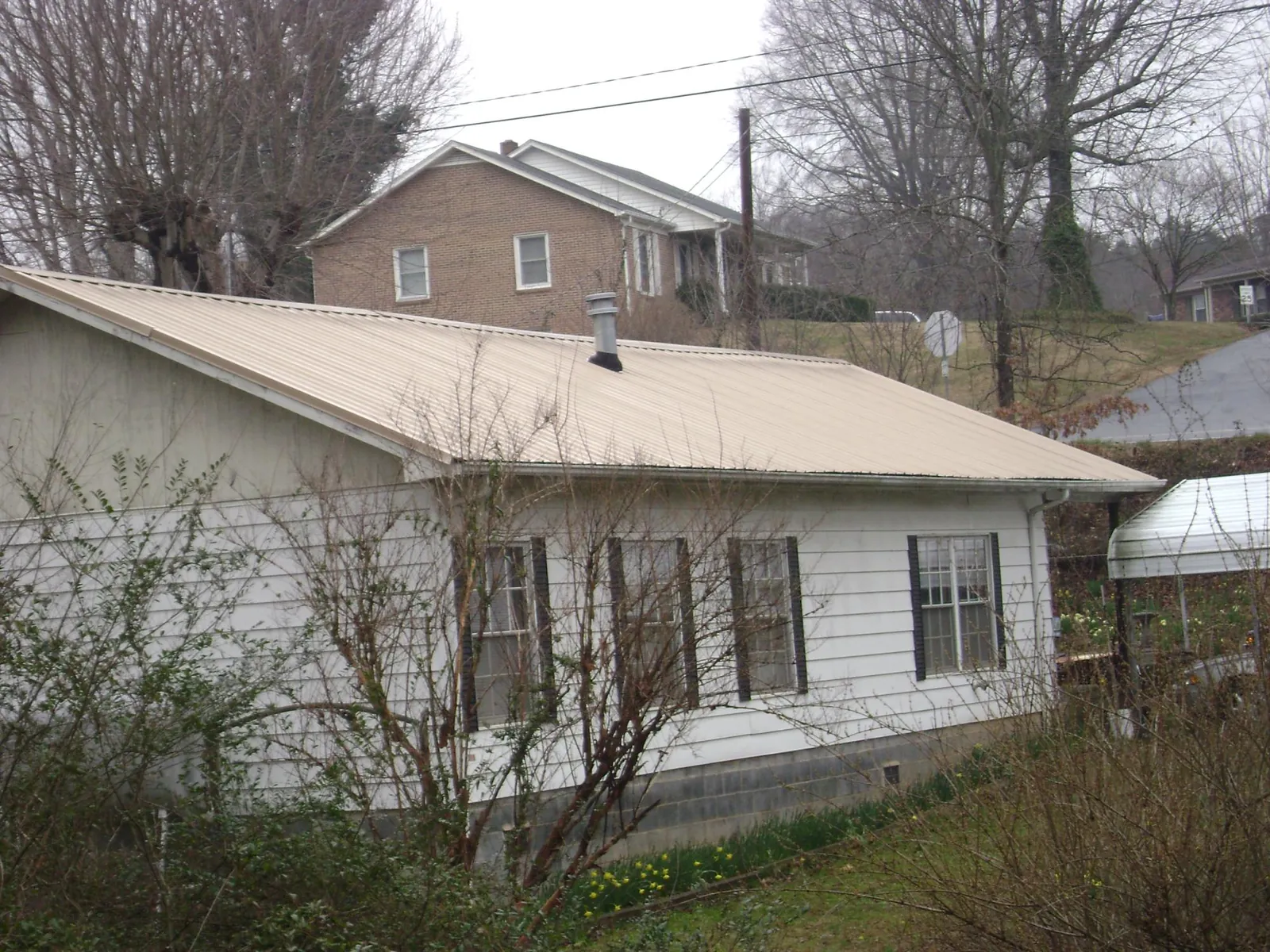 Tan metal roof on a white sided house set into a hillside — Commercial Roofing by Roofing Brothers in Cushing