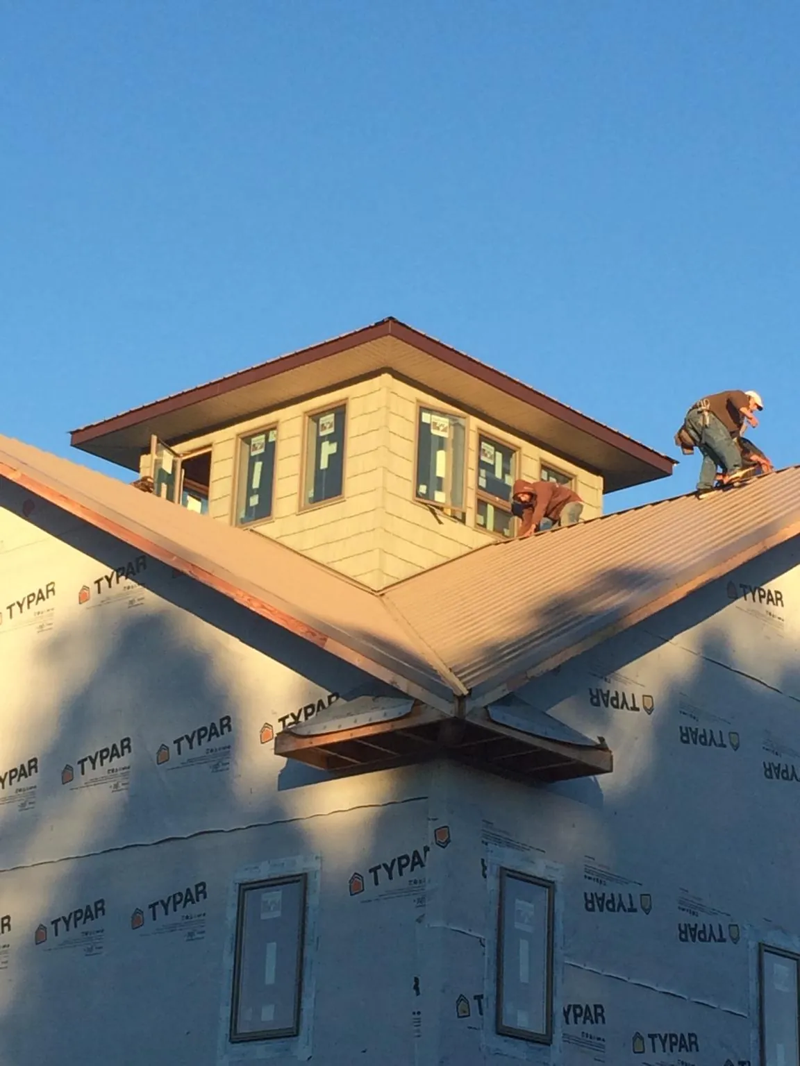 Roofers working around a rooftop cupola on a new metal roof at sunset — Roof Waterproofing in Cushing by Roofing Brothers